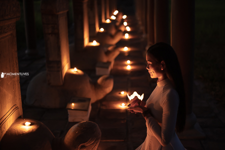 A girl in her Vietnamese traditional long dress praying with candle sticks