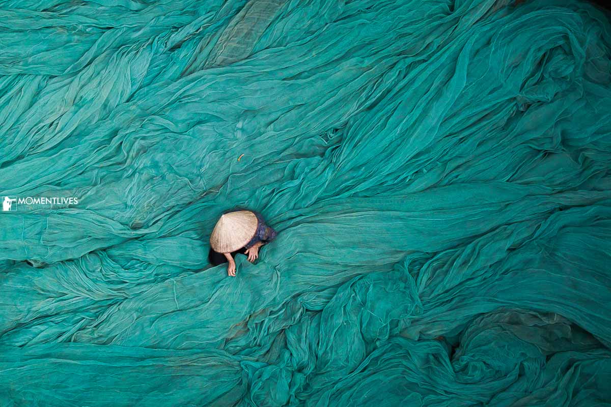 A Vietnamese woman with conical hat sitting in a sea of fishing net texture